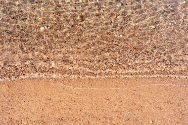 Güneşli bir günde huzurlu bir plaj sahnesini gözler önüne seren kumlu bir kıyıya vuran güneş ışığı ve küçük çakıl taşlarının yakın çekim görüntüsü..