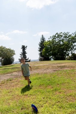 Neşeli ve kaygısız bir çocuk parlak mavi gökyüzünün altındaki canlı yeşil bir parkta eğleniyor.