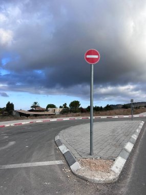 Gökyüzünde bulutlu bulutlar olan sakin bir köy yolunda girişi yasaklanmış trafik levhası yüksekte duruyor. Kırsal alan ve boş yol sakin ve izole bir atmosfer yaratır..