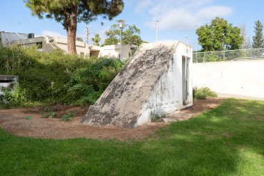 İsrail 'de yıpranmış beton bir sığınak yeşillik, ağaçlar ve patikalarla çevrili bir parkta duruyor. Dayanıklı yapı, acil durumlara dayanmak ve şehir manzarasına uyum sağlamak için inşa edilmiştir..