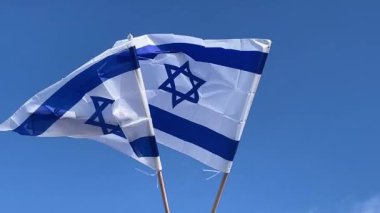 Rüzgarda dalgalanan iki İsrail bayrağı açık mavi gökyüzüne doğru hareket ve milli gurur hissini yakalıyor..