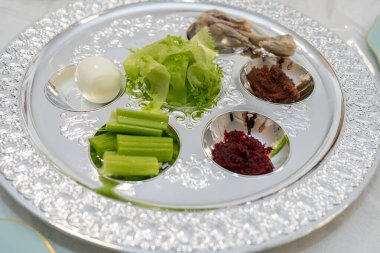 Gümüş bir Hamursuz Bayramı tabağı, Hamursuz Bayramı için sembolik yiyeceklerle ustaca düzenlenir. Tabakta kızarmış kemik, marul, maydanoz, charoset, yabanturpu ve kutlamaya uygun yumurta var..