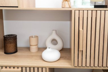 Şık bir düzenleme seramik vazolar ve dekoratif mum tutucuları içerir. Sıcak ahşap raf minimalist tasarımı ön plana çıkarıyor, odanın sıcak atmosferini arttırıyor..