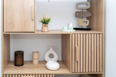 Ahşap bir rafta, minimalist bir duvara karşı dizilmiş vazolar ve bir mum gibi dekoratif eşyalardan oluşan bir koleksiyon sergileniyor. Bu rahat düzenleme modern iç dekorasyonu geliştirir.