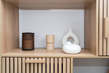 Ahşap bir rafta desenli bir kap, bir mum tutacağı ve pürüzsüz bir seramik parça da dahil olmak üzere çeşitli dekoratif eşyalar bulunur. Düzenleme görsel olarak çekici ve minimalist..