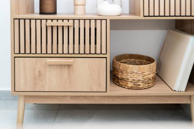 Şık bir ahşap raf dekoratif parçalar, bir dokuma sepeti ve açık bir depo alanı içerir. Doğal ışık, minimalist tasarımı ve odunun sıcak tonlarını vurgular..