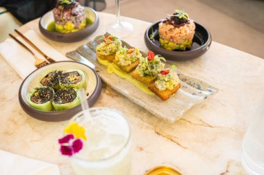 Taze deniz ürünleri, canlı sebzeler ve yaratıcı garnitürlerden oluşan lezzetli bir şekilde yerleştirilmiş küçük tabaklar, şeffaf bir bardakta sunulan çiçek kokteyli eşliğinde modern bir bistronun tadını çıkarıyor..