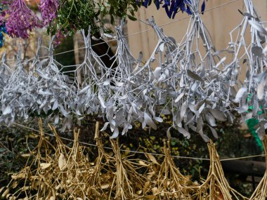 Renkli kurutulmuş otlar ve çiçekler şenlik düzeninde asılı. Gümüş ve altın ökseotu dallarının yakın çekimi bayram süsü olarak asılı, Noel geleneğini sembolize ediyor, mevsimsel kutlamaları.