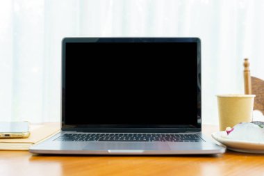 Laptop bilgisayarı, boş ekran, kağıttan yapılmış sıcak kahve ve yaban mersinli kek ve kafenin kahve dükkanının penceresinin yanındaki akıllı telefon.