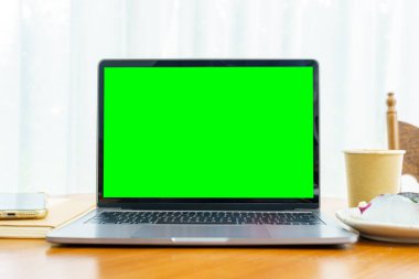 Laptop bilgisayarı, boş ekran, kağıttan yapılmış sıcak kahve ve yaban mersinli kek ve kafenin kahve dükkanının penceresinin yanındaki akıllı telefon.