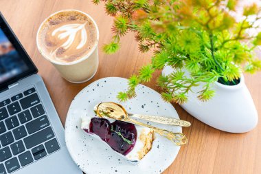 Laptop klavye yakın plan sıcak kahve sütlü sütlü latte kağıttan yapılma, ahşap masa üzerinde yabanmersinli kek. Bir kahve dükkanında, iş konseptinde kahvaltı olarak.