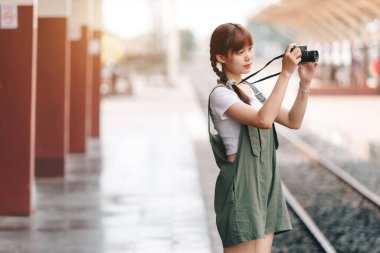 Genç Asyalı kadın gülümseyen turist kız yürüyor ve elinde kamera bekliyor tren yolculuğu tren peronunda yapılıyor Tayland, yaz tatili konsepti.