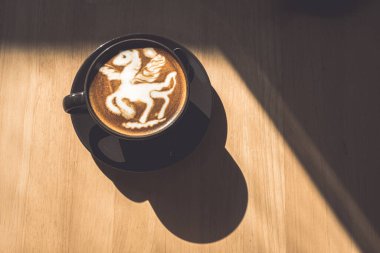 Hot coffee latte with latte art in the form of a horse milk foam in cup mug on wood desk on top view. As breakfast In a coffee shop at the cafe,during business work concept