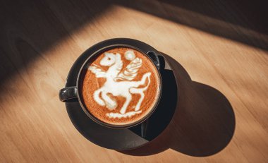 Hot coffee latte with latte art in the form of a horse milk foam in cup mug on wood desk on top view. As breakfast In a coffee shop at the cafe,during business work concept