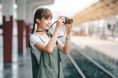 Genç Asyalı kadın gülümseyen turist kız yürüyor ve elinde kamera bekliyor tren yolculuğu tren peronunda yapılıyor Tayland, yaz tatili konsepti.