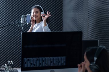 Genç Asyalı kadın vokalist kulaklık takarak profesyonel bir stüdyoda mikrofon önünde şarkı kaydettiği için Software 'ın bilgisayar monitörü kadın teknisyeni.