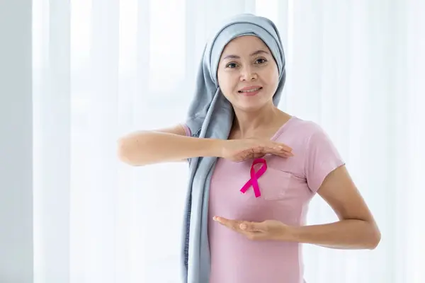 a asian women wearing headscarf disease with pink ribbon hand checking lumps on her breast for signs of breast mammary cancer isolated on at the window In the bedroom at the house,healthcare,medicine