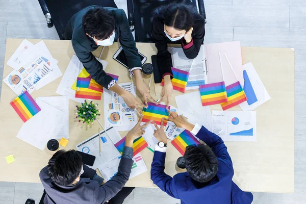 Successful workers Group of asian business partners wears hygiene protective mask with diverse genders (LGBT) putting their hands together with Paper LGBT Flag at it at meeting in the room at office,
