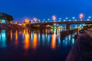 Gece vakti Tayland 'ın Phitsanulok şehrindeki parktaki Naresuan Köprüsü' nde Nan Nehri 'nin kıyılarıyla dolu güzel ışık yansıması.. 