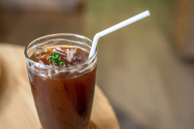 Buzlu siyah americano 'nun yakın plan resmi. İş konsepti sırasında, bahçedeki kafedeki ahşap masa masasının üzerinde cam bir fincanda.