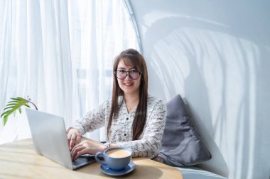 Asyalı serbest çalışanlardan memnun. İş kadını. Laptop bilgisayarı, kahve fincanı ve akıllı telefonla çalışıyor.