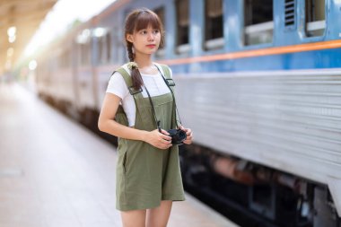 Genç Asyalı kadın gülümseyen turist kız yürüyor ve elinde kamera bekliyor tren yolculuğu tren peronunda yapılıyor Tayland, yaz tatili konsepti.