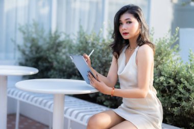 Güzel Asyalı serbest meslek sahibi insanlar yazın beyaz kolsuz elbise giyen iş kadını mankenler internet gezmek, sohbet etmek ve kafede blog yazmak için günlük işler yapıyorlar..