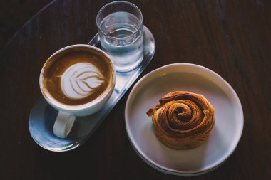 Sütlü sütlü sütlü sütlü sütlü sütlü sıcak kahve ve ahşap masa üzerinde ev yapımı Danimarka üzümü beyaz tabağı. Kafedeki bir kafede kahvaltı olarak, iş sırasında..