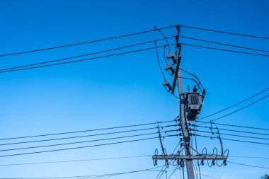 Elektrik direğinde yüksek voltajlı güç transformatörü ve Tayland 'da mavi gökyüzünün arka planında kablolar var.