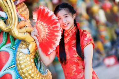 Güzel, şirin bir portre gülümseyen Asyalı genç bir kadın geleneksel Çin cheongsam süslemesi takıyor ve Tayland 'da Çin Yeni Yıl Festivali için Çin Fanning' i düzenliyor.