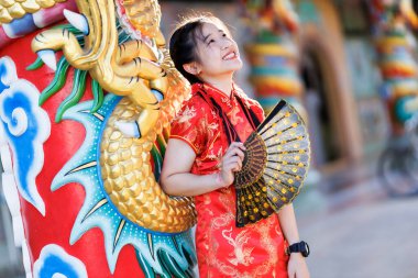 Güzel, şirin bir portre gülümseyen Asyalı genç bir kadın geleneksel Çin cheongsam süslemesi takıyor ve Tayland 'da Çin Yeni Yıl Festivali için Çin Fanning' i düzenliyor.