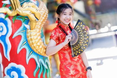 Güzel, şirin bir portre gülümseyen Asyalı genç bir kadın geleneksel Çin cheongsam süslemesi takıyor ve Tayland 'da Çin Yeni Yıl Festivali için Çin Fanning' i düzenliyor.