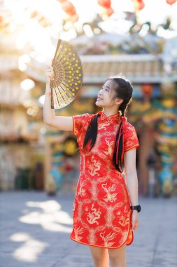 Güzel, şirin bir portre gülümseyen Asyalı genç bir kadın geleneksel Çin cheongsam süslemesi takıyor ve Tayland 'da Çin Yeni Yıl Festivali için Çin Fanning' i düzenliyor.