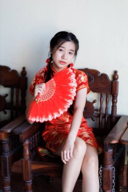 Güzel, şirin bir portre gülümseyen Asyalı genç bir kadın geleneksel Çin cheongsam süslemesi takıyor ve Tayland 'da Çin Yeni Yıl Festivali için Çin Fanning' i düzenliyor.