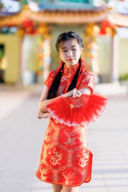 Güzel, şirin bir portre gülümseyen Asyalı genç bir kadın geleneksel Çin cheongsam süslemesi takıyor ve Tayland 'da Çin Yeni Yıl Festivali için Çin Fanning' i düzenliyor.