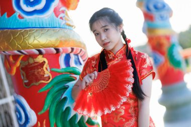 Güzel, şirin bir portre gülümseyen Asyalı genç bir kadın geleneksel Çin cheongsam süslemesi takıyor ve Tayland 'da Çin Yeni Yıl Festivali için Çin Fanning' i düzenliyor.