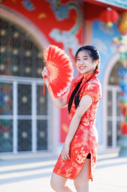 Güzel, şirin bir portre gülümseyen Asyalı genç bir kadın geleneksel Çin cheongsam süslemesi takıyor ve Tayland 'da Çin Yeni Yıl Festivali için Çin Fanning' i düzenliyor.