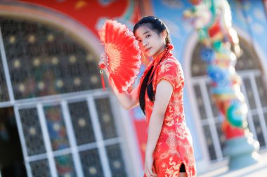 Güzel, şirin bir portre gülümseyen Asyalı genç bir kadın geleneksel Çin cheongsam süslemesi takıyor ve Tayland 'da Çin Yeni Yıl Festivali için Çin Fanning' i düzenliyor.