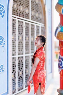 Güzel, şirin bir portre gülümseyen Asyalı genç bir kadın geleneksel Çin cheongsam süslemesi takıyor ve Tayland 'da Çin Yeni Yıl Festivali için Çin Fanning' i düzenliyor.