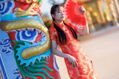 Güzel, şirin bir portre gülümseyen Asyalı genç bir kadın geleneksel Çin cheongsam süslemesi takıyor ve Tayland 'da Çin Yeni Yıl Festivali için Çin Fanning' i düzenliyor.