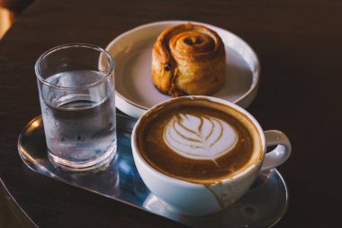 Sütlü sütlü sütlü sütlü sütlü sütlü sıcak kahve ve ahşap masa üzerinde ev yapımı Danimarka üzümü beyaz tabağı. Kafedeki bir kafede kahvaltı olarak, iş sırasında..
