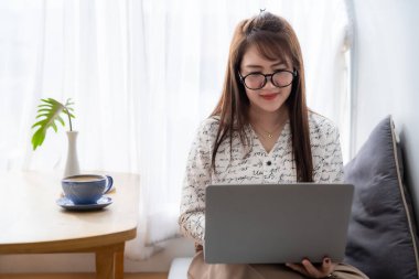 Asyalı serbest çalışanlardan memnun. İş kadını. Laptop bilgisayarı, kahve fincanı ve akıllı telefonla çalışıyor.