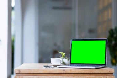 Kahve dükkanının arka planında boş ekranlı ve akıllı telefonlu dizüstü bilgisayarın bir kopyası, yeşil ekran.