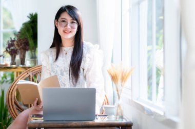 Asyalı serbest çalışanlardan memnun. İş kadını, not defteri üzerine not tutuyor. Laptop bilgisayarı, kahve fincanı ve kafeteryada akıllı telefon kullanıyor.