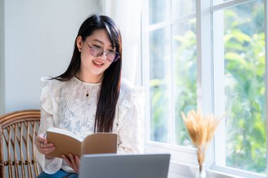 Asyalı serbest çalışanlardan memnun. İş kadını, not defteri üzerine not tutuyor. Laptop bilgisayarı, kahve fincanı ve kafeteryada akıllı telefon kullanıyor.