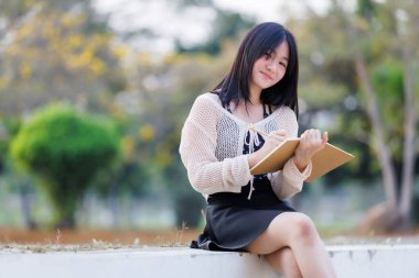 Çekici bir genç kızın portresi Asyalı gülümsüyor. Sarı Tabebuia Chrysotricha çiçeklerinde elinde bir günlük defteri tutuyor. Bahar günü Tayland 'da akşam arkaplanında parkla birlikte..