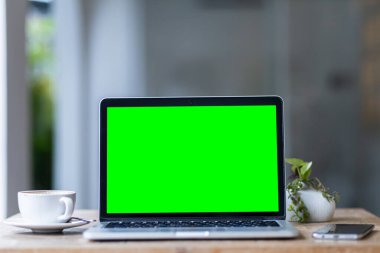 Kahve dükkanının arka planında boş ekranlı ve akıllı telefonlu dizüstü bilgisayarın bir kopyası, yeşil ekran.