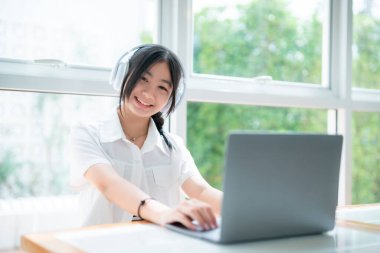 Şirin gülüşler Asyalı, kulaklık takan, müzik dinleyen, kulaklık takan, kafede çalışan bilgisayarlı çekici bir kız. Çevrimiçi eğitim, gelişim konsepti..