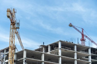 İşçiler büyük inşaat sahalarında çalışıyor ve pek çok vinç mavi gökyüzü arka planına sahip bir bina inşa ediyor..