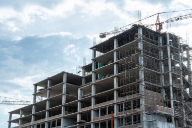 İşçiler büyük inşaat sahalarında çalışıyor ve pek çok vinç mavi gökyüzü arka planına sahip bir bina inşa ediyor..